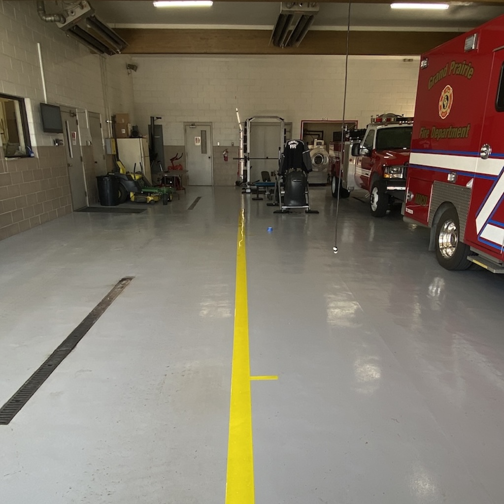 Fire station with grey epoxy floor coating with a yellow stripe and two fire trucks.