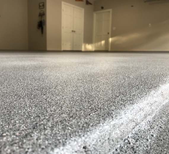 Grey epoxy and polyaspartic quartz floor coating in a garage with white doors.